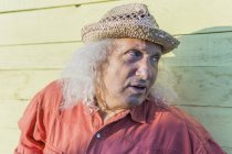 Homme âgé avec de longs cheveux gris portant un chapeau de paille regardant latéralement — Photo de stock