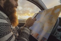 Hombre usando el teléfono inteligente en el coche, buscando direcciones en el mapa - foto de stock