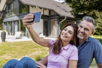 Joyeux couple assis dans le jardin de leur maison prenant un selfie — Photo de stock