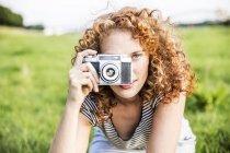 Young woman taking picture with retro camera on green meadow — Stock Photo
