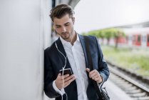 Businessman at the station with earbuds and cell phone — Stock Photo