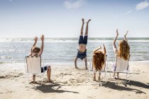 Нидерланды, Зандвоорт, семья хлопает в ладоши отцу, делая стойку на руках на пляже — стоковое фото