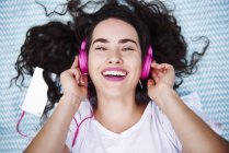 Ritratto di giovane donna felice sdraiata su una coperta ad ascoltare musica con smartphone e cuffie rosa — Foto stock