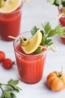 Glasses of fresh spicy tomato juice with cellery garnished with lemon slice, green olive and parsley — Stock Photo