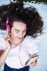 Giovane donna sorridente sdraiata su una coperta ad ascoltare musica con smartphone e cuffie rosa — Foto stock