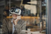 Mature businessman sitting in coffee shop, looking through VR glasses — Stock Photo