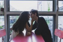 Молода пара в любові сидять на столі на вікні віч-на-віч — стокове фото