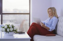 Жінка-блондинка сидить на дивані з ноутбуком. — стокове фото