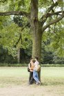 Счастливая молодая гей-пара, прислонившаяся к дереву в городском парке, глядя друг на друга — стоковое фото