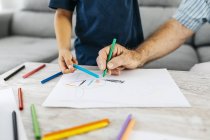 Руки дедушки и внука рисуют цветными карандашами дома — стоковое фото