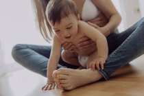 Mãe abraçando e brincando com o bebê filho no chão — Fotografia de Stock