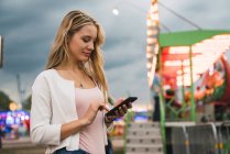 Jovem mulher usando telefone celular enquanto está em pé no parque de diversões — Fotografia de Stock