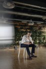 Empresario sentado en silla en oficina verde mirando el teléfono celular - foto de stock