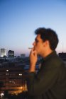 Young man smoking joint on roof in evening city — Stock Photo