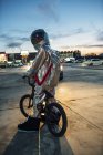 Spaceman in city at night on parking lot with bmx bike — Stock Photo