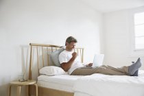 Homem maduro desfrutando de sucesso com laptop na cama — Fotografia de Stock