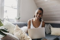Portrait of laughing woman sitting with laptop on couch at home — Stock Photo