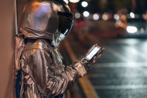 Spaceman on city street at night using cell phone — Stock Photo