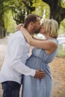 Зрелая беременная пара целуется в парке — стоковое фото