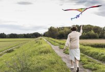 Seniorin mit Drachen in ländlicher Landschaft unterwegs — Stockfoto
