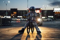 Spaceman in city at night on parking lot with bmx bike — Stock Photo