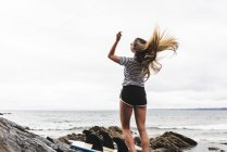 Молодая женщина с доской для серфинга танцует на пляже — стоковое фото
