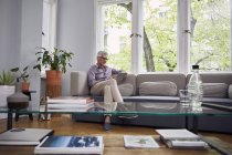Зрелый мужчина с планшетом на диване дома — стоковое фото