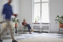 Mujer madura leyendo revista en casa con el hombre pasando por - foto de stock