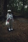 Spaceman exploring nature, using torch in dark forest — Stock Photo