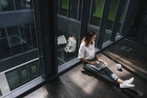 Businesswoman sitting on ground in empty office and using laptop — Stock Photo