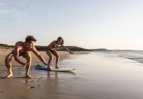 Young man showing young woman how to surf on beach — Stock Photo