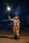 Spaceman standing outdoors at night and holding sparkler — Stock Photo