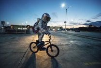 Космонавт в городе ночью на парковке с велосипедом bmx — стоковое фото