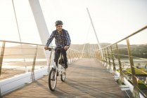 Young man riding bicycle on a bridge at sunset — Stock Photo