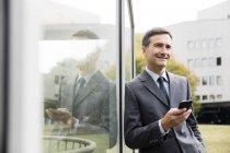 Homme d'affaires souriant avec téléphone portable appuyé contre l'avant en verre — Photo de stock