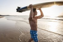 Joven caminando por la playa, llevando tabla de surf - foto de stock