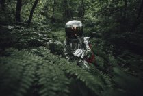 Spaceman exploring nature, examining plants in forest — Stock Photo
