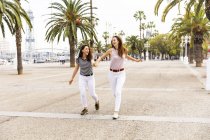 Дві щасливі друзі-жінки біжать на набережній з долонями — стокове фото
