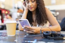 Молода жінка сидить за столом і використовує мобільний телефон — стокове фото