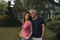 Sonriente pareja madura de pie en el jardín de la casa - foto de stock