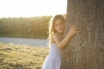 Девушка опирается на ствол дерева в летний вечер — стоковое фото