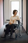 Donna d'affari disabile seduta in sedia a rotelle in ufficio e distogliendo lo sguardo — Foto stock
