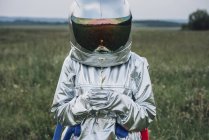 Spaceman holding flower in green meadow — Stock Photo