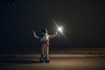 Spaceman standing on road at night holding sparkler — Stock Photo