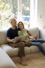 Щаслива зріла пара сидить на дивані вдома з мобільним телефоном і ноутбуком — стокове фото