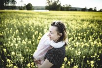 Kleines Mädchen auf dem Arm der Mutter im blühenden Rapsfeld — Stockfoto