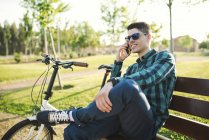 Young man telephoning with smartphone on park bench — Stock Photo
