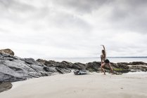 Jeune femme avec planche de surf étirant sur la plage — Photo de stock