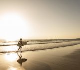 Young man running on beach, carrying surfboard — Stock Photo