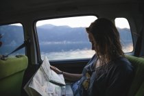 Mujer joven sentada en el asiento trasero en un coche y mirando el mapa - foto de stock